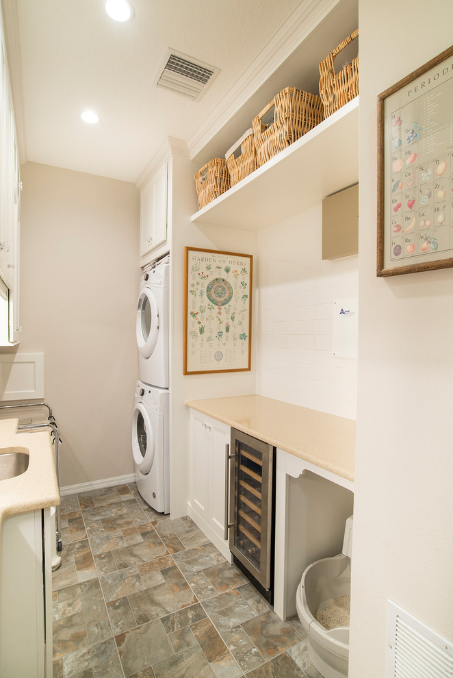 オーランドにある小さなヴィクトリアン調のおしゃれな洗濯室 (ll型、アンダーカウンターシンク、落し込みパネル扉のキャビネット、白いキャビネット、ラミネートカウンター、白い壁、上下配置の洗濯機・乾燥機、グレーの床) の写真