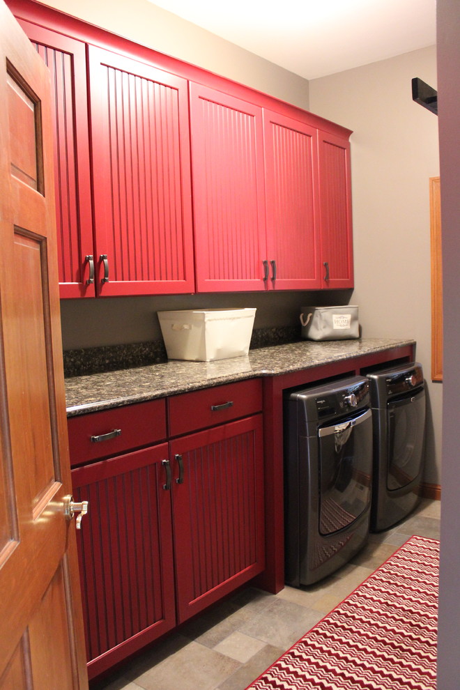 Inredning av en klassisk mellanstor parallell tvättstuga enbart för tvätt, med luckor med infälld panel, röda skåp, bänkskiva i kvarts, grå väggar, klinkergolv i keramik och en tvättmaskin och torktumlare bredvid varandra