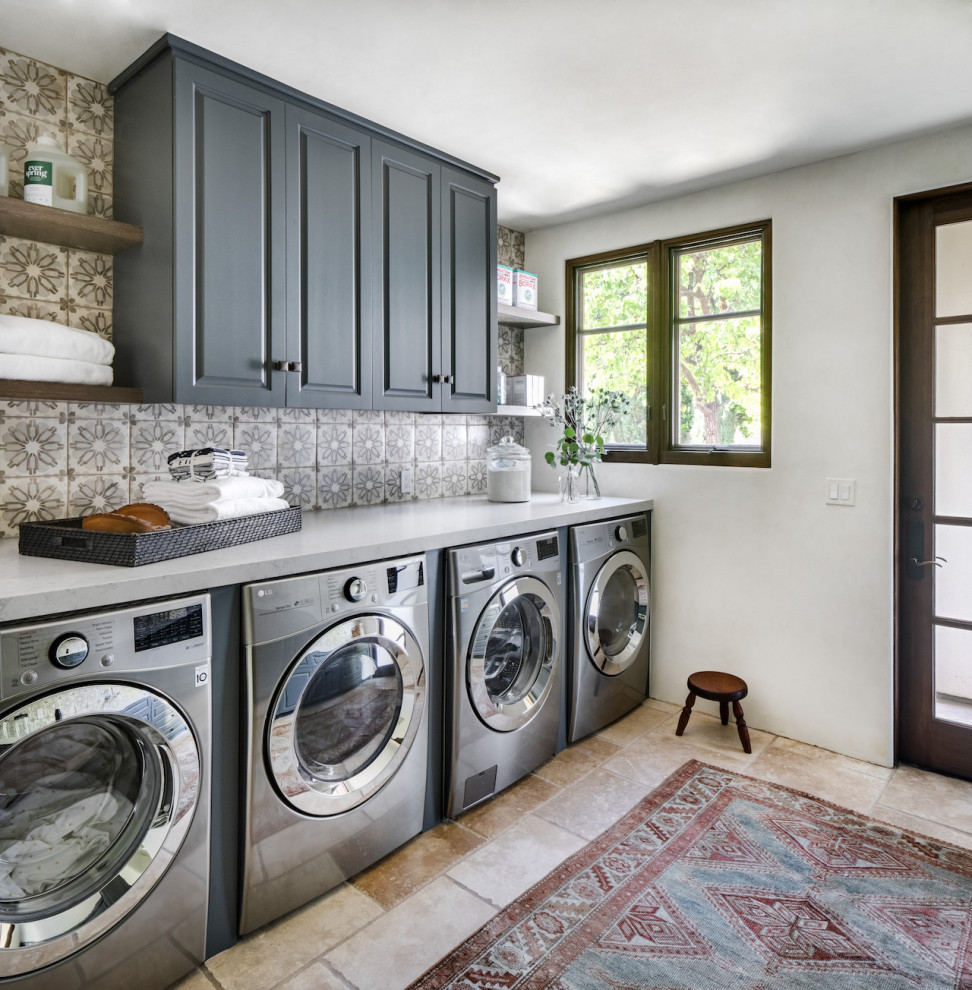 Idéer för mellanstora medelhavsstil linjära grått tvättstugor enbart för tvätt, med luckor med upphöjd panel, grå skåp, bänkskiva i kvarts, vita väggar, travertin golv, en tvättmaskin och torktumlare bredvid varandra och beiget golv