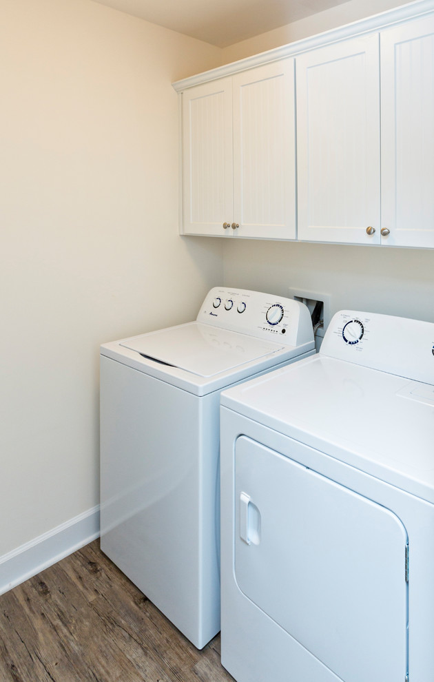 Immagine di una lavanderia multiuso stile marino di medie dimensioni con ante a persiana, ante bianche, pareti beige, parquet scuro, lavatrice e asciugatrice affiancate e pavimento marrone