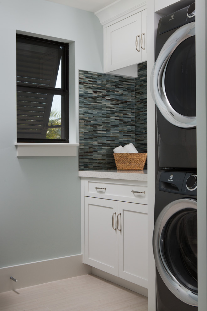 Immagine di una sala lavanderia costiera con ante in stile shaker, ante bianche, pareti blu, parquet chiaro, lavatrice e asciugatrice a colonna, pavimento beige e top beige