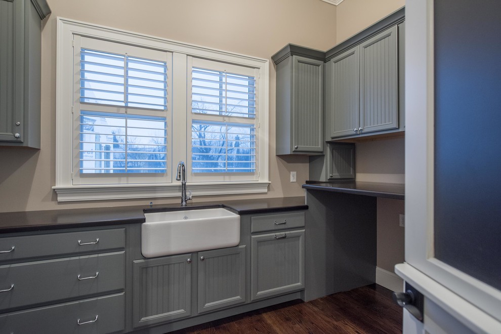 Inspiration for a mid-sized transitional dark wood floor and brown floor laundry room remodel in Columbus with a farmhouse sink, gray cabinets, solid surface countertops, gray walls and recessed-panel cabinets