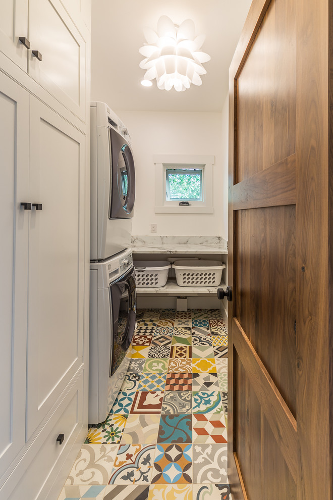 Modelo de cuarto de lavado campestre con puertas de armario blancas, encimera de laminado, paredes blancas y lavadora y secadora apiladas