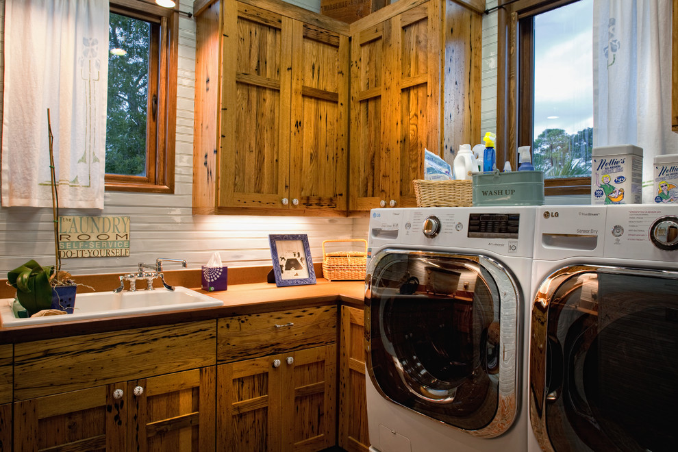 Immagine di una sala lavanderia rustica di medie dimensioni con lavello da incasso, ante con bugna sagomata, ante in legno scuro, lavatrice e asciugatrice affiancate e pareti bianche