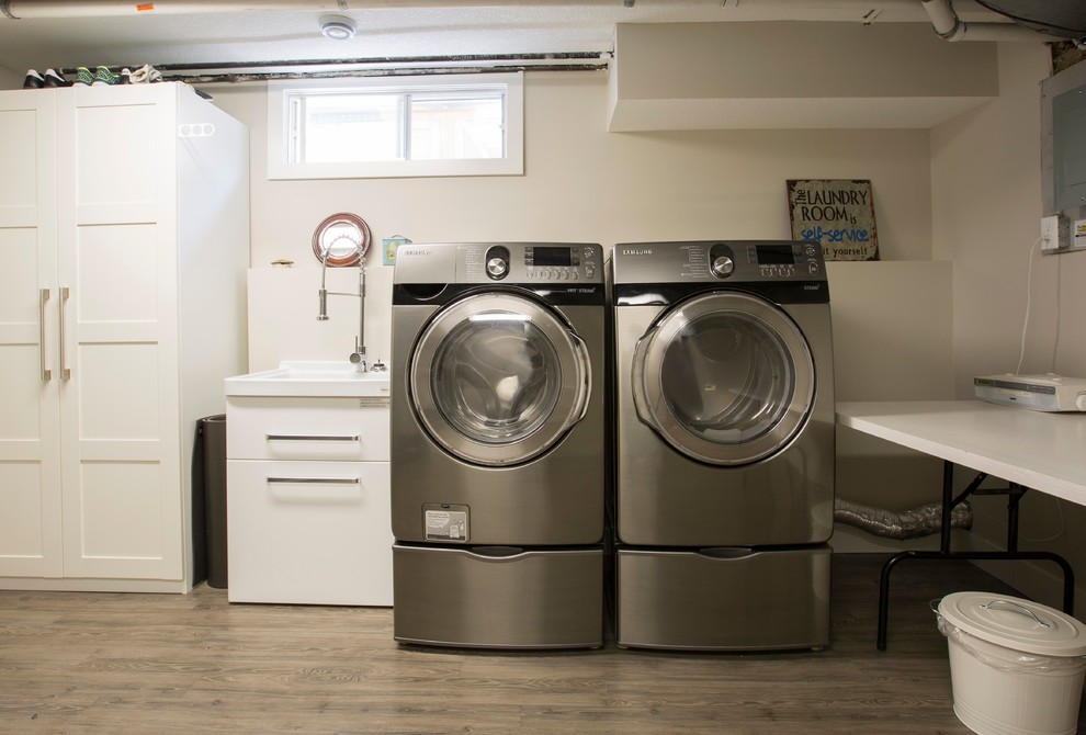 Immagine di una sala lavanderia industriale di medie dimensioni con lavatoio, ante lisce, pareti bianche, parquet scuro, lavatrice e asciugatrice affiancate e pavimento marrone