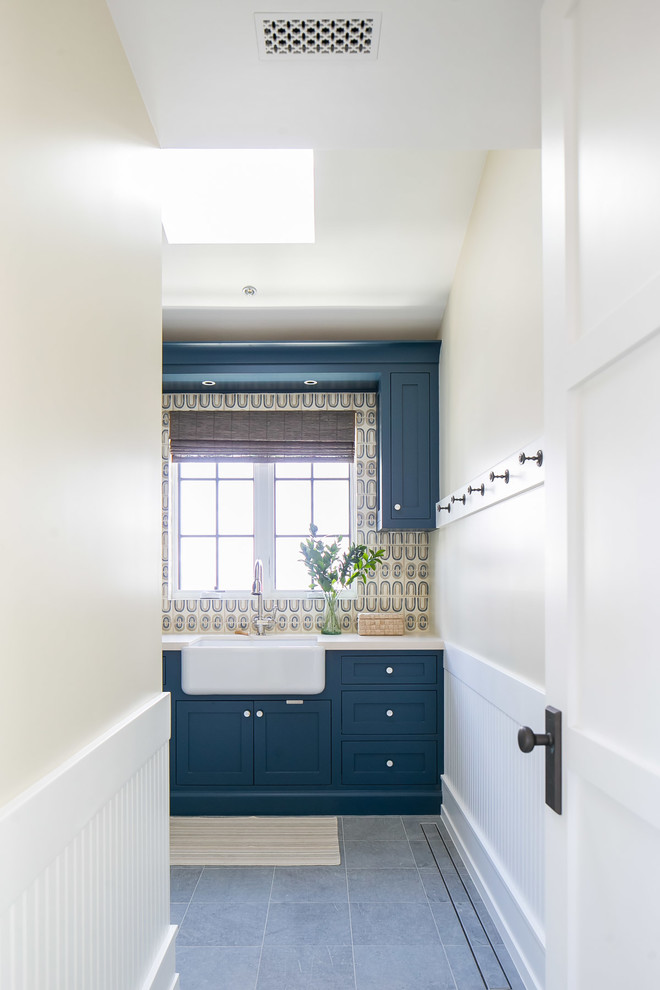 Example of a large island style l-shaped gray floor dedicated laundry room design in Orange County with a farmhouse sink, shaker cabinets, blue cabinets, a side-by-side washer/dryer, beige countertops and beige walls