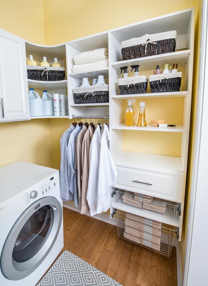 Ejemplo de lavadero en L de tamaño medio con armarios con paneles con relieve, puertas de armario blancas, paredes amarillas, suelo de bambú y lavadora y secadora juntas