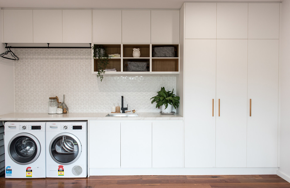Photo of a medium sized contemporary single-wall utility room in Melbourne with a submerged sink, recessed-panel cabinets, white cabinets, engineered stone countertops, white walls, dark hardwood flooring, a side by side washer and dryer, brown floors and white worktops.
