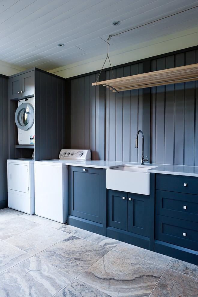 Klassisk inredning av en stor tvättstuga enbart för tvätt, med en rustik diskho, skåp i shakerstil, marmorbänkskiva, grå väggar, travertin golv, en tvättmaskin och torktumlare bredvid varandra och blå skåp