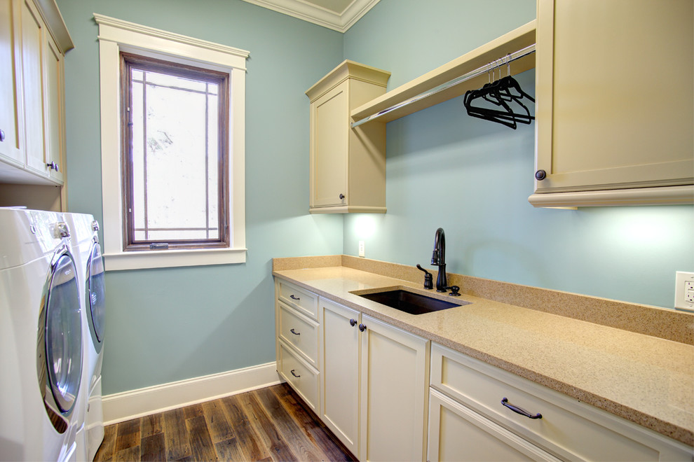 Foto de lavadero tradicional con fregadero encastrado, armarios estilo shaker, puertas de armario beige, paredes azules, suelo de madera en tonos medios y lavadora y secadora juntas