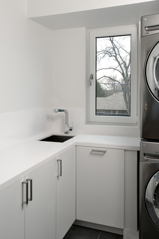 Moderne Waschküche in L-Form mit Waschbecken, flächenbündigen Schrankfronten, weißen Schränken, Quarzit-Arbeitsplatte, weißer Wandfarbe, Waschmaschine und Trockner gestapelt und weißer Arbeitsplatte in Toronto