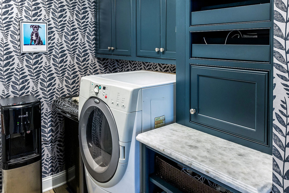 Medium sized traditional l-shaped separated utility room in DC Metro with shaker cabinets, blue cabinets, beige walls, engineered stone countertops and a stacked washer and dryer.