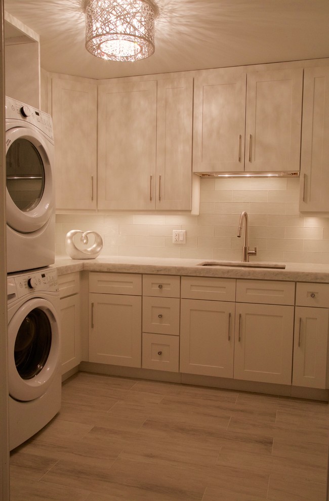Inspiration for a medium sized contemporary l-shaped utility room in Phoenix with a submerged sink, shaker cabinets, white cabinets, marble worktops, white walls, light hardwood flooring, a stacked washer and dryer and beige floors.
