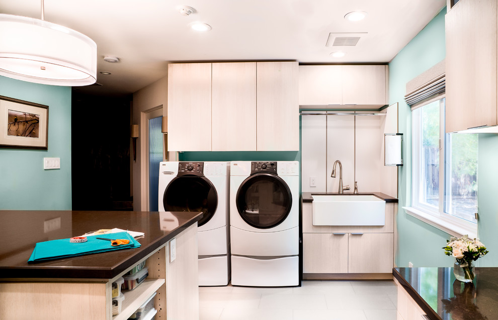 Inspiration for a large contemporary u-shaped utility room in San Francisco with a belfast sink, light wood cabinets, quartz worktops, blue walls, a side by side washer and dryer, porcelain flooring, white floors, brown worktops and flat-panel cabinets.