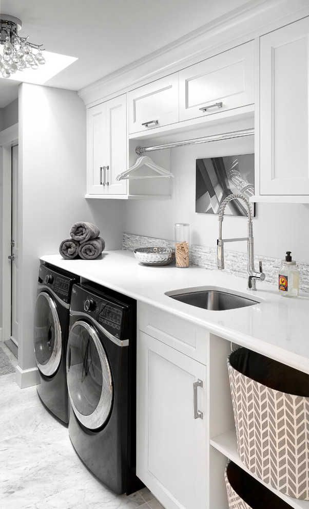 Exempel på en klassisk vita vitt tvättstuga, med en undermonterad diskho, luckor med infälld panel, vita skåp, vita väggar och en tvättmaskin och torktumlare bredvid varandra