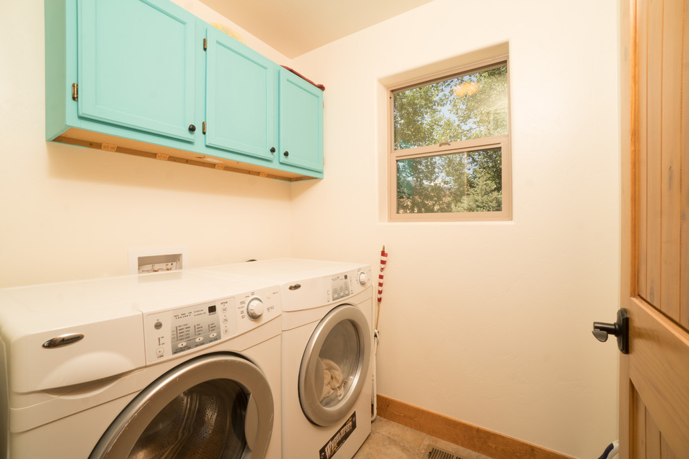 Inredning av en amerikansk mellanstor tvättstuga enbart för tvätt, med luckor med upphöjd panel, beige väggar, en tvättmaskin och torktumlare bredvid varandra, flerfärgat golv, blå skåp och klinkergolv i keramik