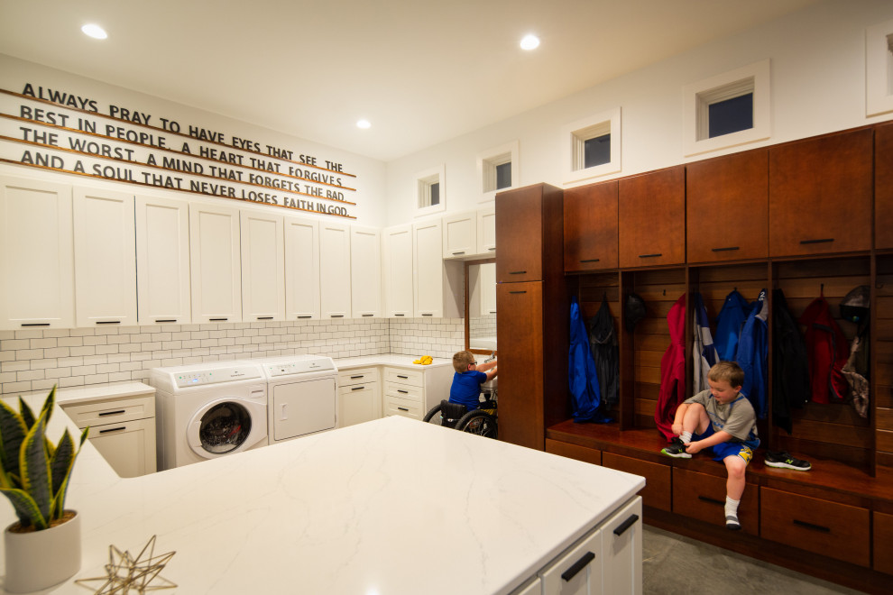 This is an example of a large modern u-shaped utility room in Other with white cabinets, white walls, concrete flooring, a side by side washer and dryer and white worktops.