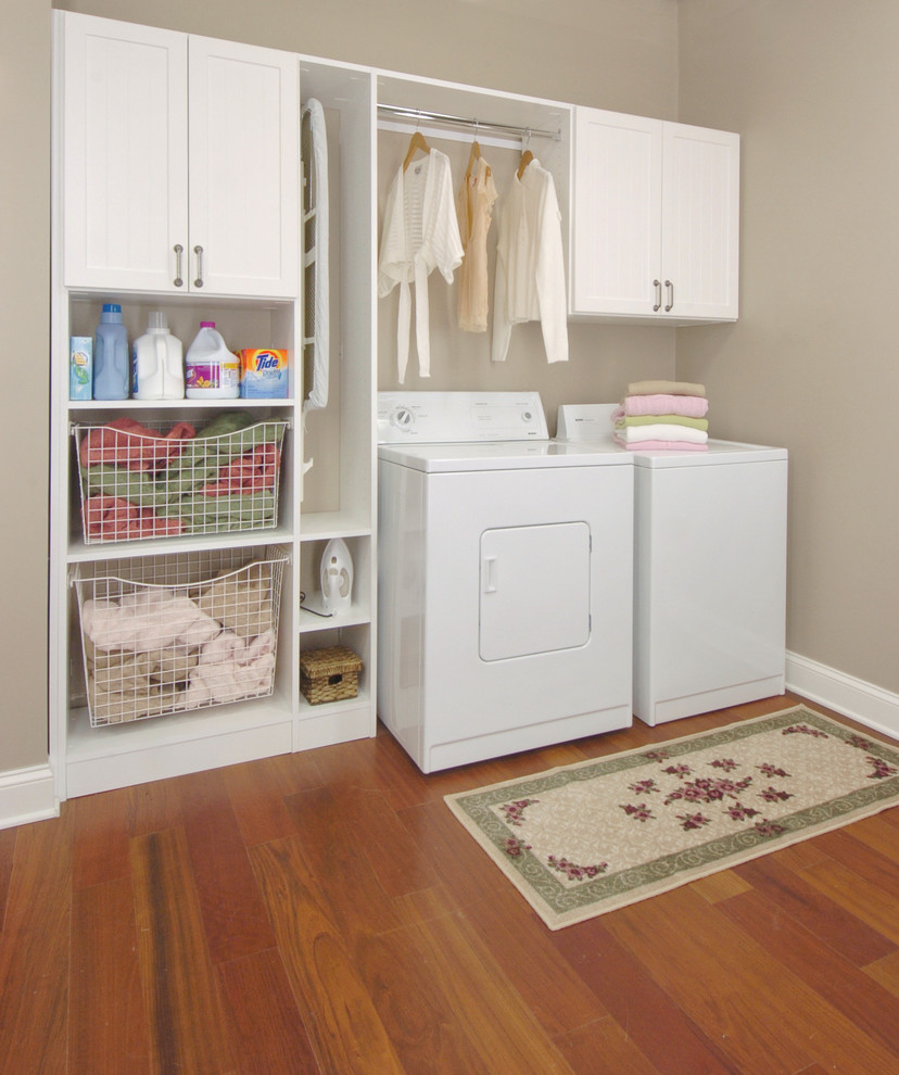 Ejemplo de cuarto de lavado lineal clásico de tamaño medio con armarios estilo shaker, puertas de armario blancas, paredes beige, suelo de madera oscura, lavadora y secadora juntas y suelo marrón
