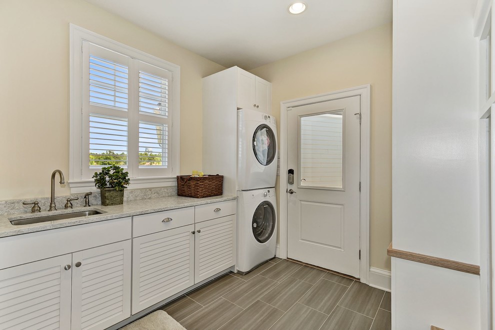 Immagine di una lavanderia multiuso minimalista di medie dimensioni con lavello sottopiano, ante a persiana, ante bianche, top in granito, lavatrice e asciugatrice a colonna e top beige
