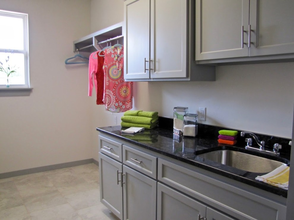 Photo of a medium sized traditional single-wall separated utility room in Oklahoma City with a single-bowl sink, shaker cabinets, green cabinets, beige walls, a side by side washer and dryer, beige floors and black worktops.