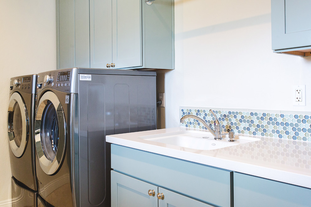Exempel på en stor medelhavsstil parallell tvättstuga enbart för tvätt, med en undermonterad diskho, skåp i shakerstil, blå skåp, bänkskiva i kvarts, vita väggar, travertin golv och en tvättmaskin och torktumlare bredvid varandra