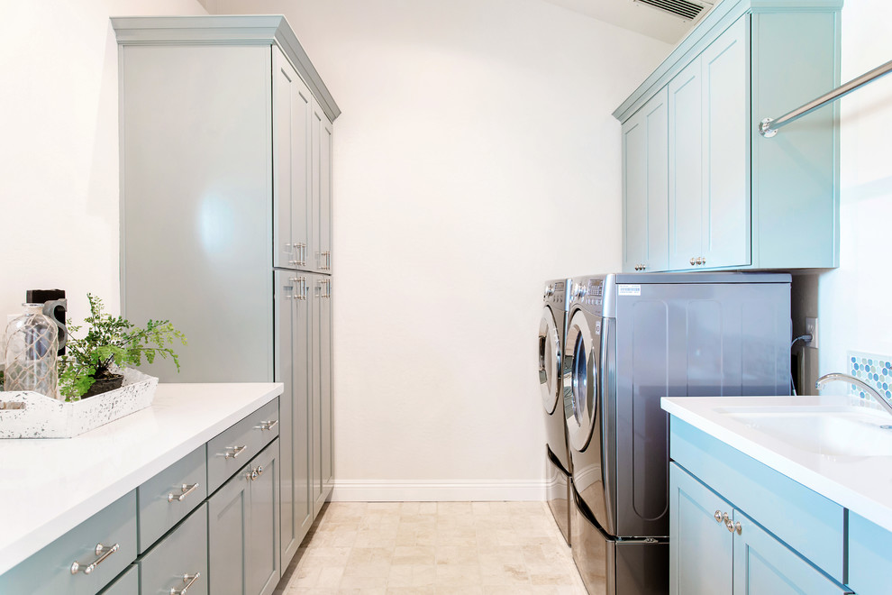 Idéer för stora medelhavsstil parallella tvättstugor enbart för tvätt, med en undermonterad diskho, skåp i shakerstil, blå skåp, bänkskiva i kvarts, vita väggar, travertin golv och en tvättmaskin och torktumlare bredvid varandra
