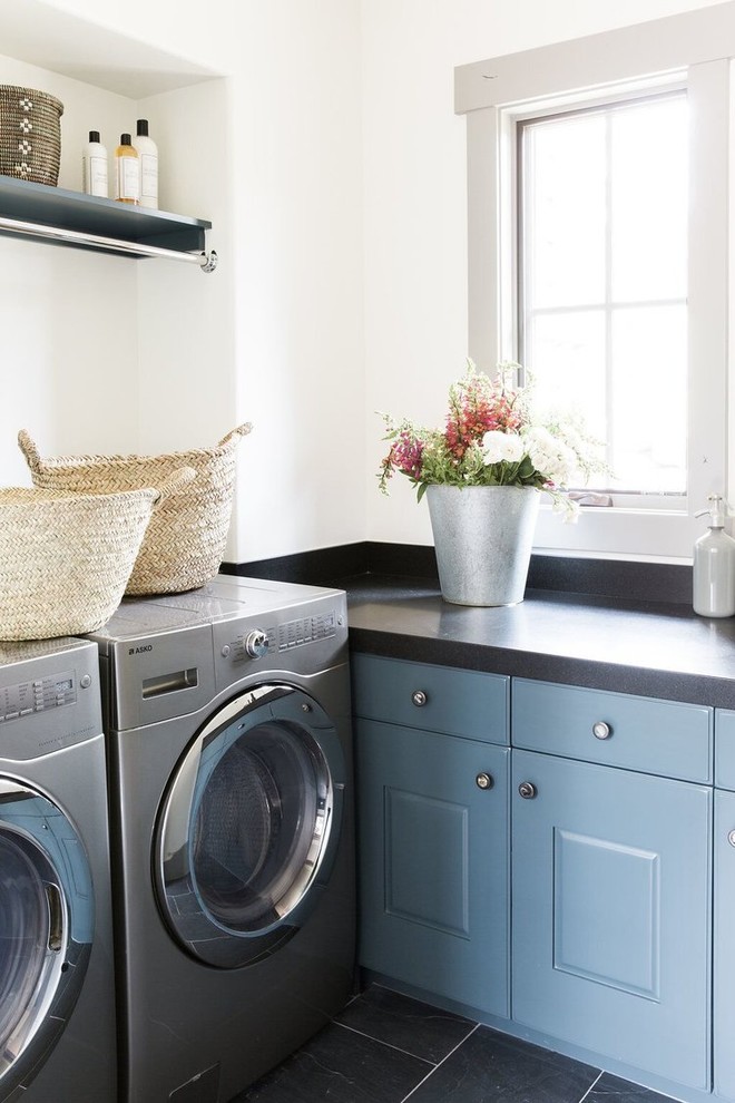 Ejemplo de cuarto de lavado clásico renovado con puertas de armario azules, paredes blancas, lavadora y secadora juntas y suelo gris