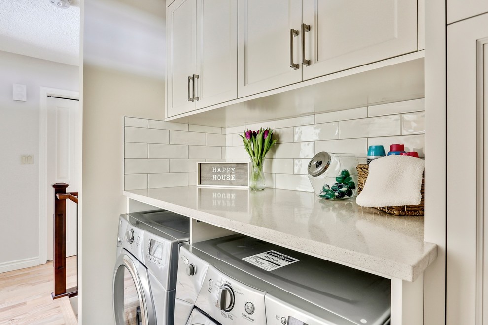 Klassisk inredning av en mellanstor vita linjär vitt tvättstuga enbart för tvätt, med luckor med infälld panel, vita skåp, bänkskiva i kvarts, vita väggar, klinkergolv i porslin, en tvättmaskin och torktumlare bredvid varandra och grått golv