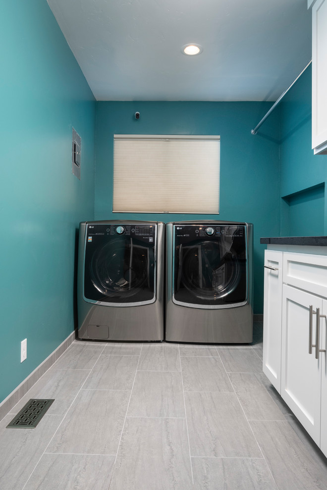 Inredning av en modern stor svarta l-formad svart tvättstuga enbart för tvätt, med en undermonterad diskho, skåp i shakerstil, vita skåp, granitbänkskiva, klinkergolv i porslin, en tvättmaskin och torktumlare bredvid varandra, grått golv och blå väggar