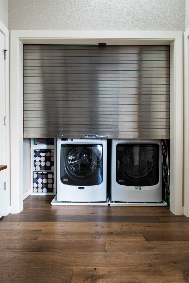 Foto på ett mellanstort funkis l-format grovkök, med vita skåp, träbänkskiva, grå väggar, mellanmörkt trägolv och en tvättmaskin och torktumlare bredvid varandra