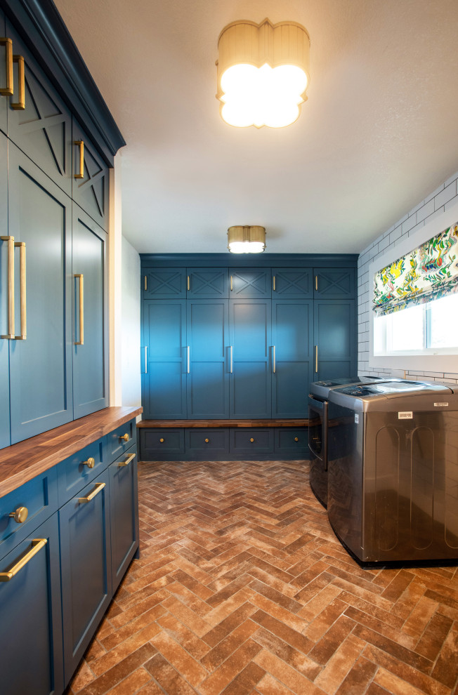 Inspiration for a small traditional utility room in Denver with shaker cabinets, blue cabinets, wood worktops, white walls, brick flooring, a side by side washer and dryer, red floors and brown worktops.