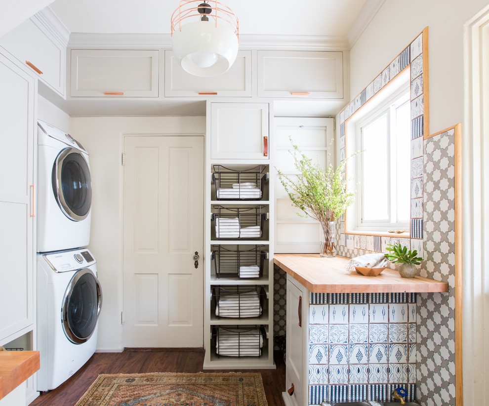 Inspiration for a mid-sized farmhouse dark wood floor laundry room remodel in Los Angeles with shaker cabinets, gray cabinets, wood countertops, white walls, a stacked washer/dryer and beige countertops