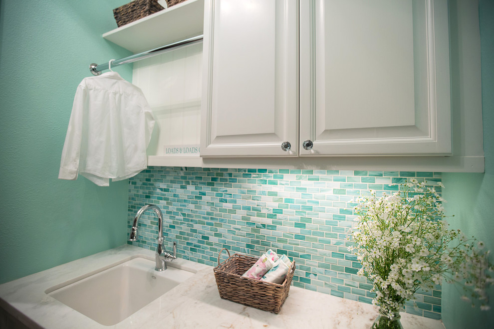 Example of a mid-sized beach style galley porcelain tile and beige floor dedicated laundry room design in Los Angeles with an undermount sink, raised-panel cabinets, white cabinets, marble countertops, blue walls and a stacked washer/dryer