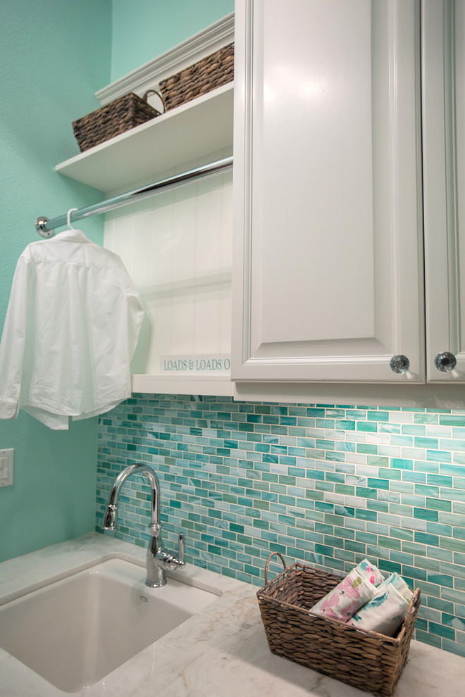Zweizeilige, Mittelgroße Klassische Waschküche mit Unterbauwaschbecken, profilierten Schrankfronten, weißen Schränken, Marmor-Arbeitsplatte, blauer Wandfarbe, Porzellan-Bodenfliesen, Waschmaschine und Trockner gestapelt und beigem Boden in Los Angeles