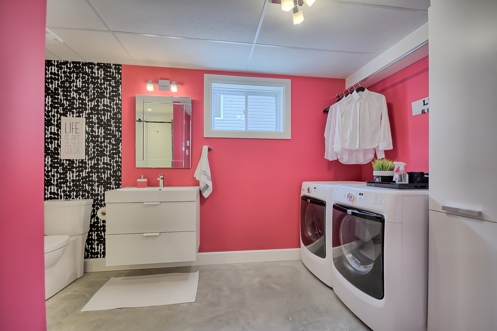 Modern inredning av ett mellanstort linjärt grovkök, med rosa väggar, betonggolv och en tvättmaskin och torktumlare bredvid varandra