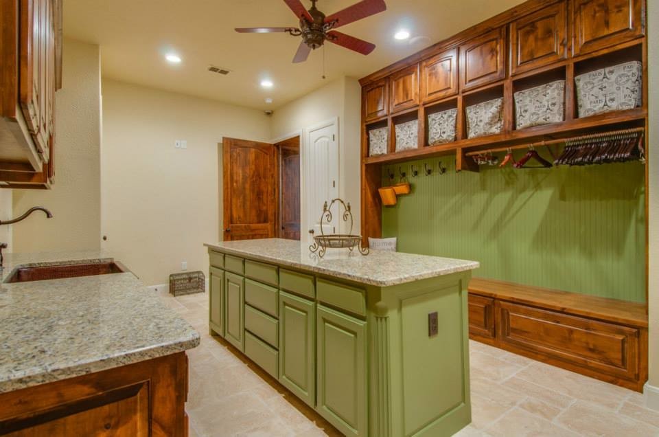 Example of a mid-sized mountain style single-wall travertine floor and beige floor dedicated laundry room design in Dallas with a farmhouse sink, raised-panel cabinets, dark wood cabinets, granite countertops, beige walls and a stacked washer/dryer