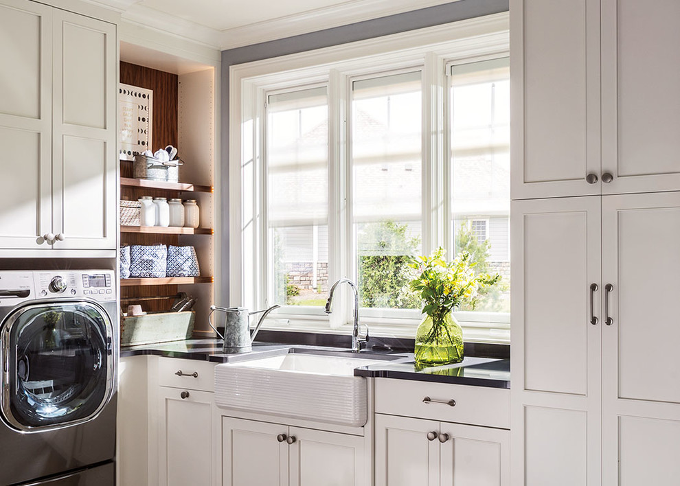 Dedicated laundry room - mid-sized transitional l-shaped dedicated laundry room idea in Chicago with a farmhouse sink, shaker cabinets, white cabinets, solid surface countertops, a side-by-side washer/dryer and black countertops