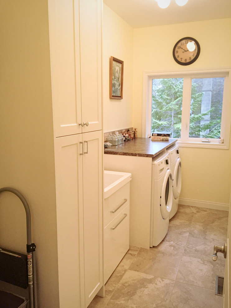 Bild på en lantlig bruna parallell brunt liten tvättstuga, med en allbänk, skåp i shakerstil, vita skåp, laminatbänkskiva, gula väggar, klinkergolv i porslin, en tvättmaskin och torktumlare bredvid varandra och beiget golv