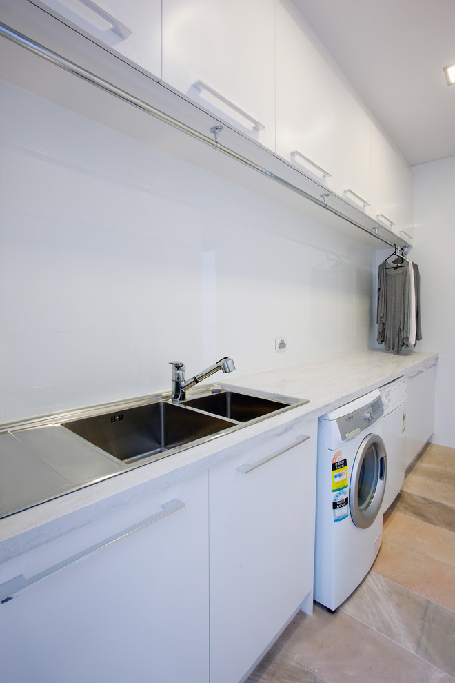 Moderner Hauswirtschaftsraum mit Doppelwaschbecken, flächenbündigen Schrankfronten, weißen Schränken, Mineralwerkstoff-Arbeitsplatte, weißer Wandfarbe, Waschmaschine und Trockner nebeneinander und grauer Arbeitsplatte in Perth