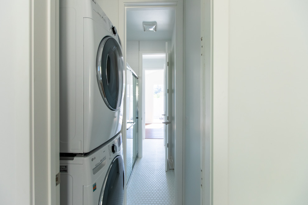 Immagine di una piccola lavanderia costiera con pareti bianche, pavimento con piastrelle in ceramica, lavatrice e asciugatrice a colonna e pavimento bianco