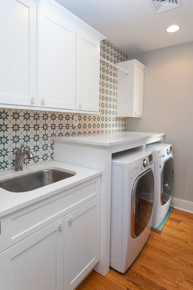 Exempel på en liten klassisk vita linjär vitt tvättstuga enbart för tvätt, med en undermonterad diskho, skåp i shakerstil, vita skåp, bänkskiva i kvarts, grå väggar, mellanmörkt trägolv, en tvättmaskin och torktumlare bredvid varandra och brunt golv