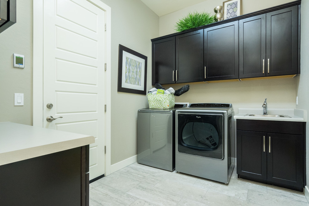 Large contemporary single-wall utility room in Phoenix with a built-in sink, recessed-panel cabinets, black cabinets, composite countertops, beige walls, porcelain flooring, a side by side washer and dryer and beige floors.