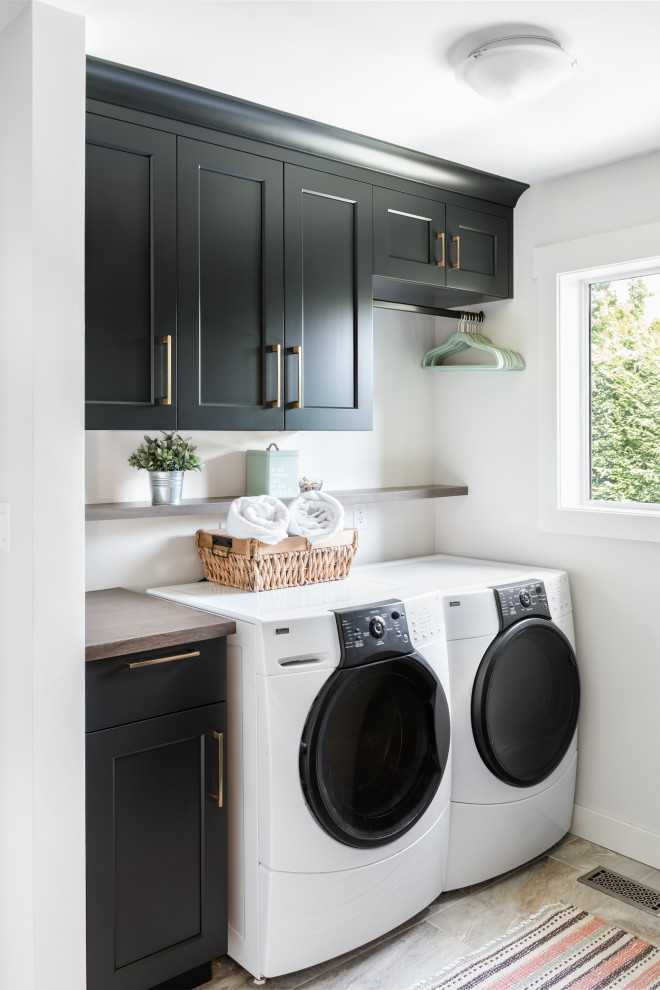 Imagen de cuarto de lavado lineal tradicional renovado con armarios estilo shaker, puertas de armario negras, paredes blancas, lavadora y secadora juntas, suelo gris y encimeras marrones