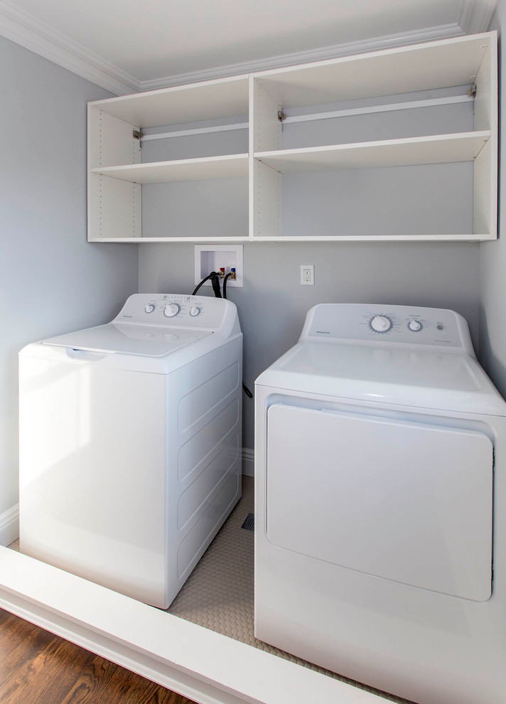 ニューヨークにある中くらいなコンテンポラリースタイルのおしゃれな洗濯室 (濃色無垢フローリング、左右配置の洗濯機・乾燥機、ll型、オープンシェルフ、白いキャビネット、グレーの壁) の写真