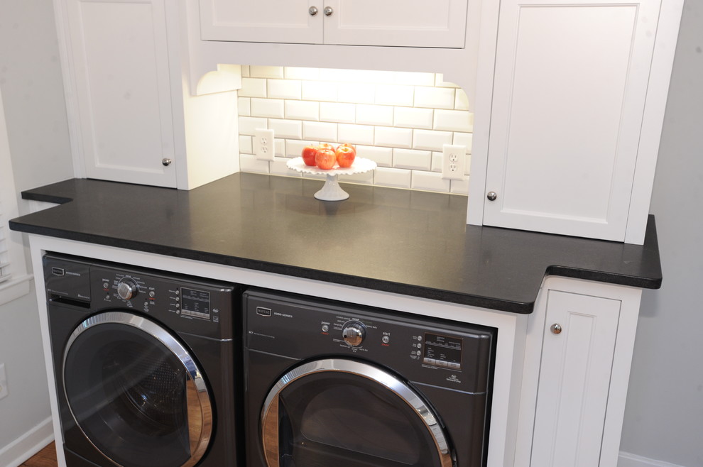 Inspiration for a large classic u-shaped utility room in Atlanta with a submerged sink, white cabinets, granite worktops, white splashback, metro tiled splashback, light hardwood flooring, recessed-panel cabinets, grey walls, a side by side washer and dryer and brown floors.