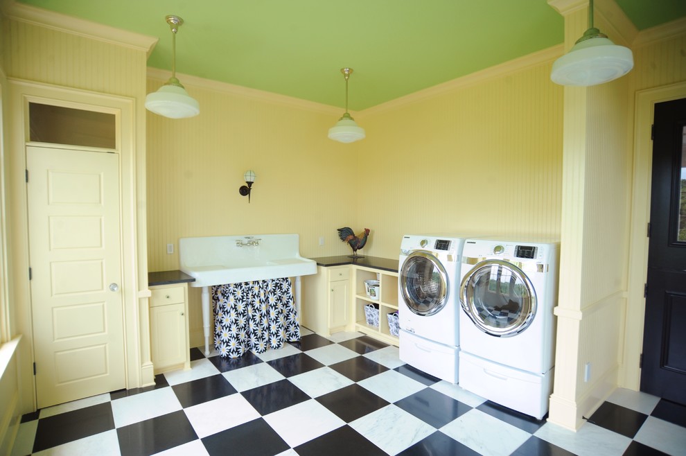 Zweizeilige, Große Klassische Waschküche mit Landhausspüle, Schrankfronten mit vertiefter Füllung, gelben Schränken, Granit-Arbeitsplatte, gelber Wandfarbe, Marmorboden, Waschmaschine und Trockner nebeneinander und weißem Boden in Sonstige