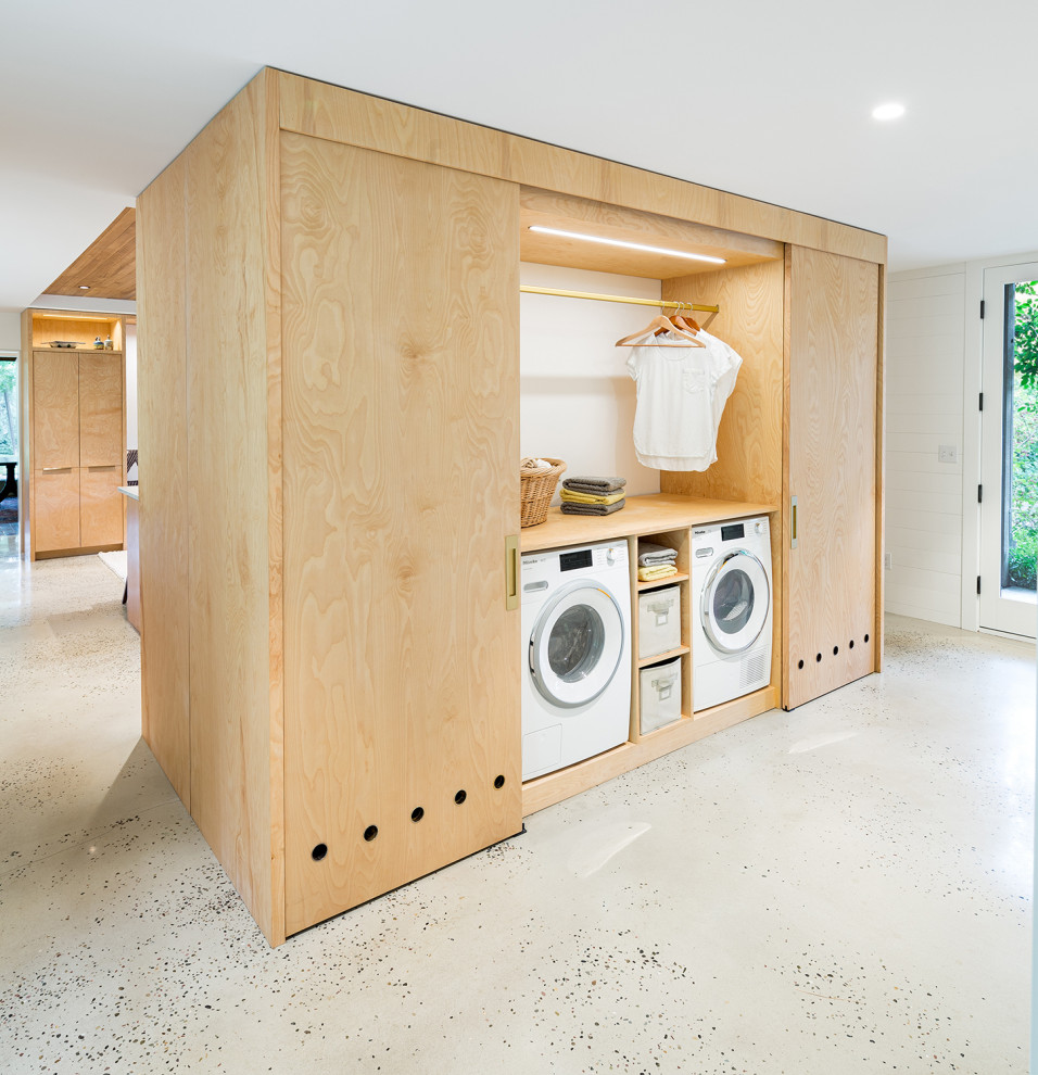 Ispirazione per una lavanderia multiuso minimalista con ante lisce, ante in legno chiaro, top in legno, pavimento in cemento, lavatrice e asciugatrice nascoste e pavimento grigio