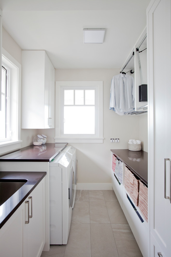 Mid-sized trendy galley porcelain tile and beige floor dedicated laundry room photo in Vancouver with an undermount sink, recessed-panel cabinets, white cabinets, quartz countertops, white walls and a side-by-side washer/dryer
