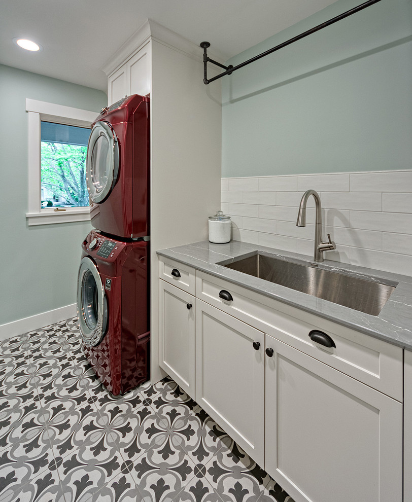 Minimalistisk inredning av en liten grå parallell grått tvättstuga enbart för tvätt, med en undermonterad diskho, släta luckor, vita skåp, bänkskiva i kvarts, gröna väggar, klinkergolv i porslin och en tvättpelare