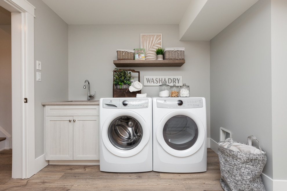 Immagine di una lavanderia multiuso tradizionale di medie dimensioni con lavello sottopiano, ante in stile shaker, ante in legno chiaro, pareti grigie, lavatrice e asciugatrice affiancate, pavimento beige e top beige